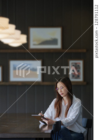 side view of Asian woman wearing eyeglasses using tablet for work in the morning on the wooden dining table, working from home concept side view of Asian woman wearing eyeglasses using tablet for work in the morning on the wooden dining table, working from home concept 128701112