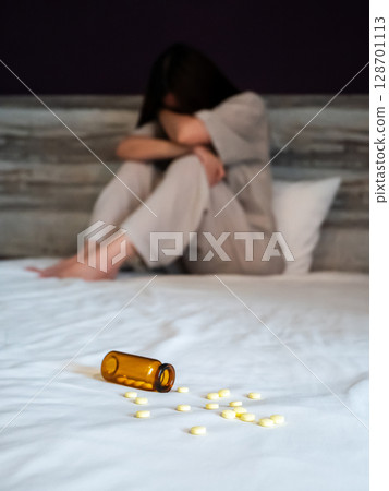 woman suffer from insomnia, focus on sleeping pills foreground on bed. front view of woman in stress in bedroom with sleep disorder. insomnia depression treatment concept 128701113