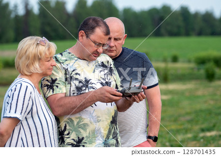 Group of mature people watching drone remote control screen in park 128701435