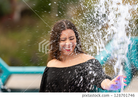 Joyful Woman Playing in Splashing Water at Outdoor Park in Bright Sunshine Joyful Woman Playing in Splashing Water at Outdoor Park in Bright Sunshine 128701746