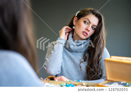reflection of a woman in mirror choosing and trying different jewelry, soft focus, closeup reflection of a woman in mirror choosing and trying different jewelry, soft focus, closeup 128702055