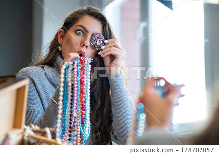reflection of a woman in mirror choosing and trying different jewelry, soft focus, closeup reflection of a woman in mirror choosing and trying different jewelry, soft focus, closeup 128702057