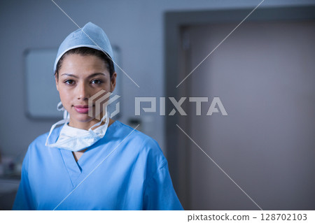 Female medical professional standing in prep room, wearing scrubs, cap and mask around neck Female medical professional standing in prep room, wearing scrubs, cap and mask around neck 128702103