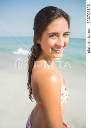 Smiling woman turning over shoulder on sandy shoreline, wearing floral bikini with ocean waves Smiling woman turning over shoulder on sandy shoreline, wearing floral bikini with ocean waves 128702128