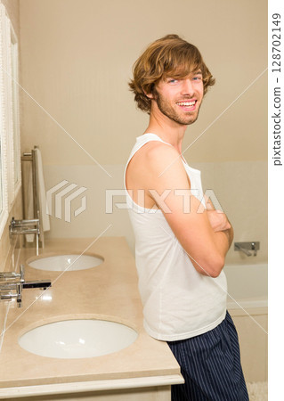 Smiling man leaning against marble countertop in bathroom, with double sinks, copy space 128702149