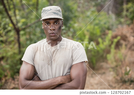 Standing African American man crossing arms in forested area, with camouflage cap and dirty t shirt 128702167