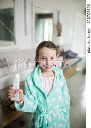 Smiling female child standing in modern bathroom by double white sinks, holding toothpaste tube 128702168