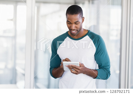 Tapping mid adult African American man using tablet in modern office corridor with glass partitions Tapping mid adult African American man using tablet in modern office corridor with glass partitions 128702171