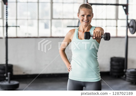 Lifting dumbbell, woman performing shoulder raise in gym with grid windows, showing strength Lifting dumbbell, woman performing shoulder raise in gym with grid windows, showing strength 128702189