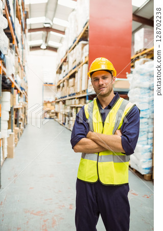 Male warehouse worker scanning inventory in aisle, with safety helmet and vest, copy space 128702238