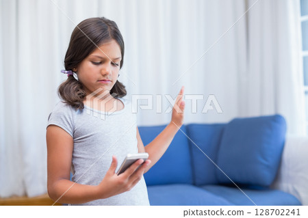 Holding smartphone and making stop gesture girl child standing in living room, copy space Holding smartphone and making stop gesture girl child standing in living room, copy space 128702241