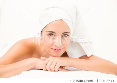 Relaxing woman resting on spa table in wellness room, with towel turban and white sheet 128702244