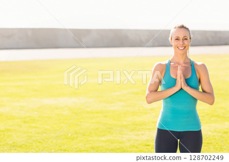 Woman holding prayer pose and smiling in wide grassy field under bright sky, copy space 128702249