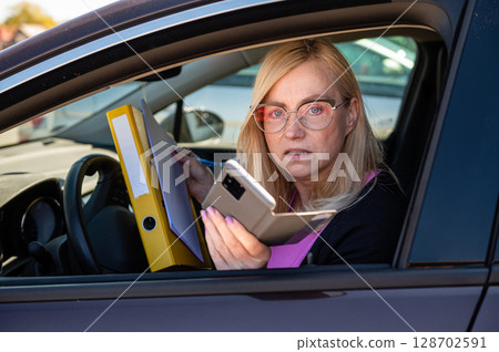 middle aged blonde business woman in glasses in car working with documents, mobile technology concept 128702591