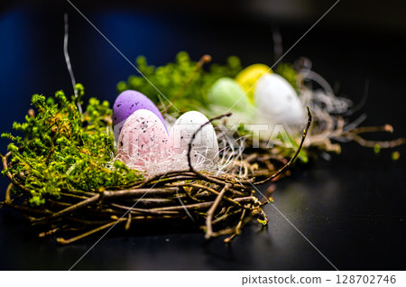 nest with colored Easter eggs isolated on a dark defocused background, easter decorations, close-up nest with colored Easter eggs isolated on a dark defocused background, easter decorations, close-up 128702746