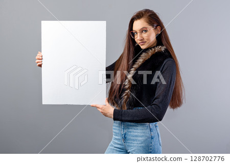 portrait of young teenager woman showing blank signboard with copy space, isolated on gray 128702776