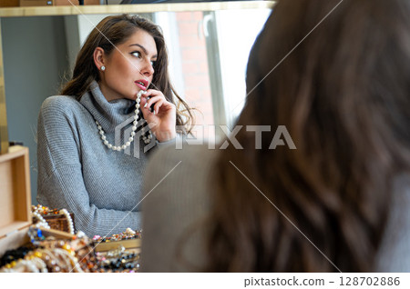 reflection of a woman in mirror choosing and trying different jewelry, soft focus, closeup reflection of a woman in mirror choosing and trying different jewelry, soft focus, closeup 128702886