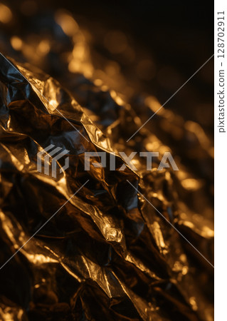Abstract Close-Up of Gleaming Crumpled Gold Foil Highlighted by Warm Dramatic Lighting 128702911