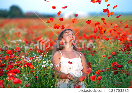 cute girl wearing white dress in summer blooming poppy field playing under evening sun 128703285
