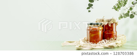 Probiotic food banner. Eco friendly still life with pickled or fermented vegetables in glass jars on textile bag on blue background with leaves and shadows. Home food preserving or canning. Copy space Probiotic food banner. Eco friendly still life with pickled or fermented vegetables in glass jars on textile bag on blue background with leaves and shadows. Home food preserving or canning. Copy space 128703386