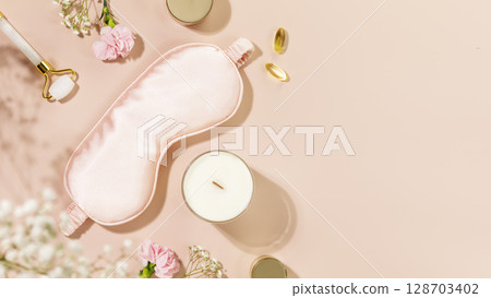 Self care flat lay with mask for sleep, candle and beauty products on pink background with flowers. Concept of Relaxing at home, Me time, take care, healthy and good sleeping. Copy space 128703402