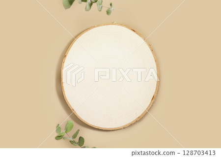 Wooden round empty podium for montage of your products. Product display on beige background with eucalyptus leaves. Concept of scene stage for natural products or promotion sale. Flat lay 128703413