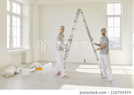 Team of house painters looking at camera holding paint rollers and going to paint the wall 128703474
