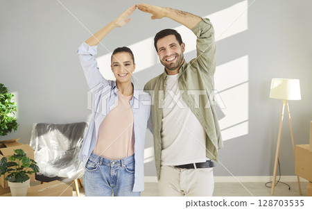 Happy young couple forming roof shape with hands over heads, celebrating purchase of new apartment. Happy young couple forming roof shape with hands over heads, celebrating purchase of new apartment. 128703535