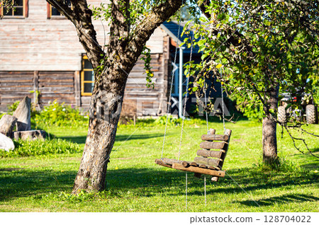 a swinging wooden bench hung in a tree with chains in the garden of a country house 128704022