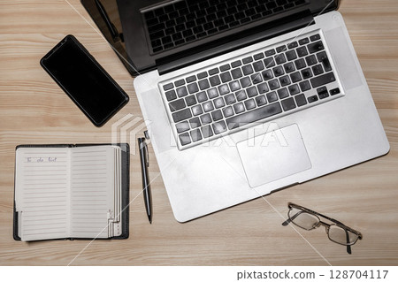 Desk with laptop, eyeglasses, notepad, smartphone, and pen on a wooden table. Top view with copy space. Flat lay - image Desk with laptop, eyeglasses, notepad, smartphone, and pen on a wooden table. Top view with copy space. Flat lay - image 128704117