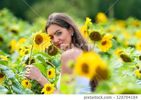 sexy young brunette with long hair in sunflower field on summer day, woman surrounded by sunflowers 128704184