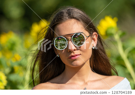 pretty sensual young brunette in sunglasses in a field of blooming sunflowers, young woman portrait 128704189