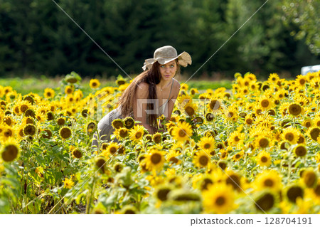 beautiful woman walking in a field of sunflowers in a linean country style dress and straw hat 128704191