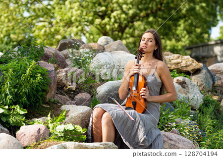 portrait of a young beautiful violinist on a pile of boulders near an old country house portrait of a young beautiful violinist on a pile of boulders near an old country house 128704194
