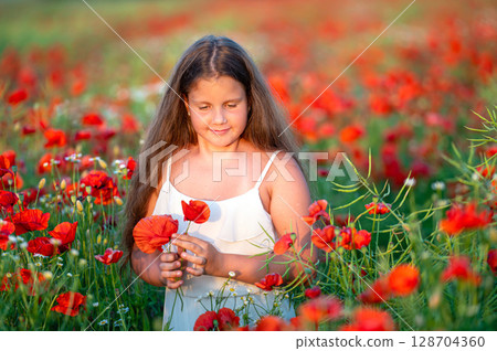 cute girl wearing white dress in summer blooming poppy field walking under evening sun 128704360