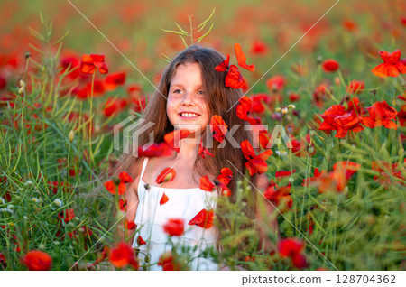 cute girl wearing white dress in summer blooming poppy field walking under evening sun 128704362