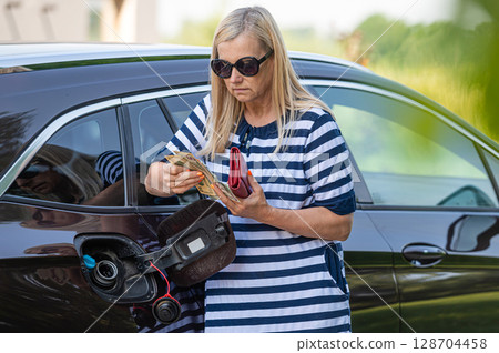 worried woman with cash at the open car tank, the concept of rising fuel prices worried woman with cash at the open car tank, the concept of rising fuel prices 128704458