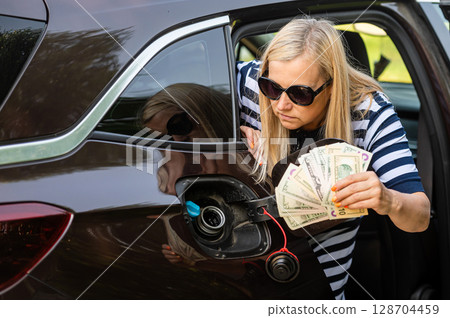 worried woman with cash in hands looking at the open car tank, the concept of rising fuel prices worried woman with cash in hands looking at the open car tank, the concept of rising fuel prices 128704459