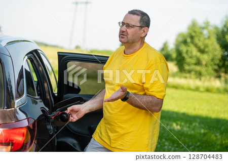 worried and surprised emotional man at open car fuel tank, fuel price rise concept 128704483