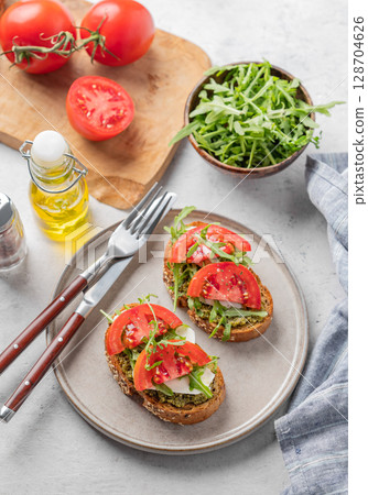 Healthy sesame toast with tomatoes, mozzarella, arugula and pesto on plate on light background Healthy sesame toast with tomatoes, mozzarella, arugula and pesto on plate on light background 128704626