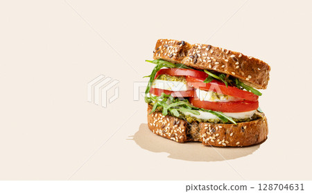 Sandwich of grain bread with tomatoes, mozzarella, arugula and pesto on bright beige background Sandwich of grain bread with tomatoes, mozzarella, arugula and pesto on bright beige background 128704631