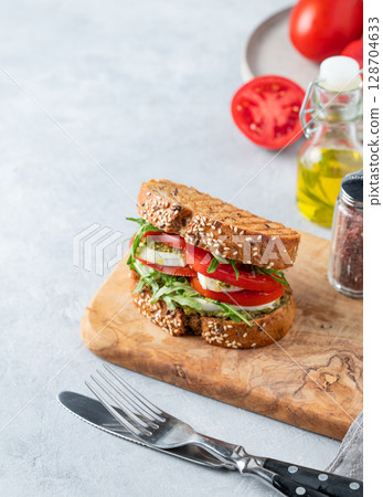 Sandwich of grain bread with tomatoes, mozzarella, arugula and pesto on a wooden board Sandwich of grain bread with tomatoes, mozzarella, arugula and pesto on a wooden board 128704633