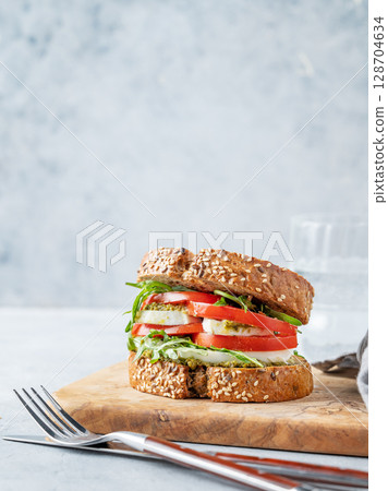 Sandwich of grain bread with fresh tomatoes mozzarella, arugula and pesto on a wooden board 128704634