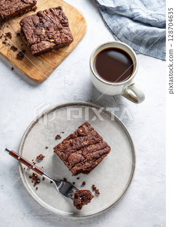 Chocolate brownie on a plate on a light background with cup of freshly brewed coffee and napkin. 128704635