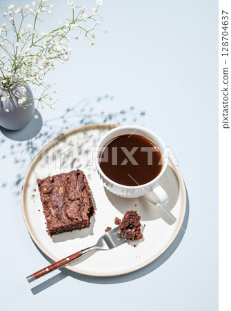 Chocolate brownie on a plate on a blue background with cup of freshly brewed coffee Chocolate brownie on a plate on a blue background with cup of freshly brewed coffee 128704637