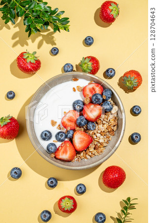 Natural yogurt with granola, blueberry and strawberry in a bowl on a yellow background Natural yogurt with granola, blueberry and strawberry in a bowl on a yellow background 128704643