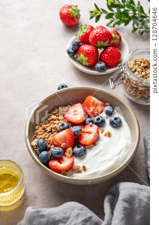 Natural greek yogurt with granola, blueberry and strawberry in a bowl on a light background 128704646