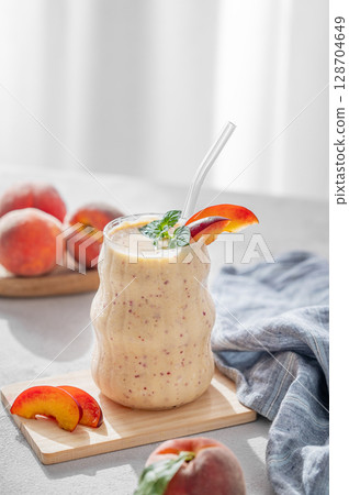 Smoothie with peach and banana in a glass on a light background near window with tropical fruit Smoothie with peach and banana in a glass on a light background near window with tropical fruit 128704649
