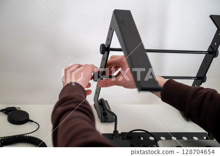person adjusting ergonomic metal laptop stand on white desk in home office person adjusting ergonomic metal laptop stand on white desk in home office 128704654
