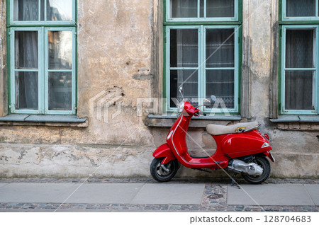 Red vintage scooter on the sidewalk in front of an old brick house 128704683